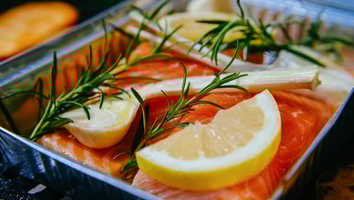 Fresh salmon fillets arranged in a metal tray, topped with lemon wedges and sprigs of rosemary, ready for cooking