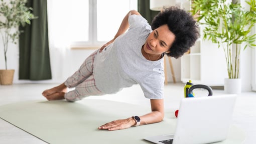 A adult woman performing an isometric side plank exercise on a yoga mat indoors.
