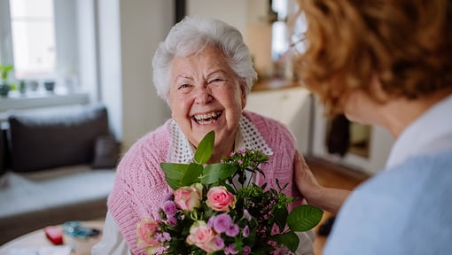 Person presenting a vibrant bouquet of pink and purple flowers to another very happy individual