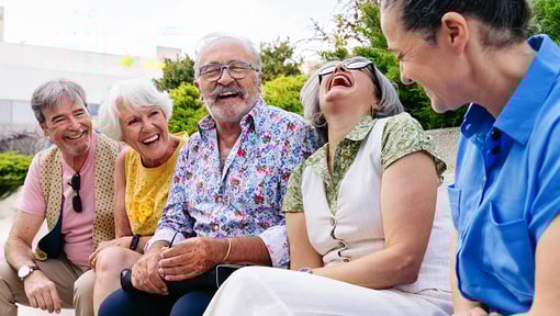 Group of people sitting close together outdoors on a bench, engaged in conversation and sharing a lighthearted moment