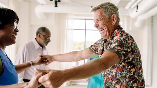 Two people holding hands and dancing in a bright indoor space, with another person visible in the background