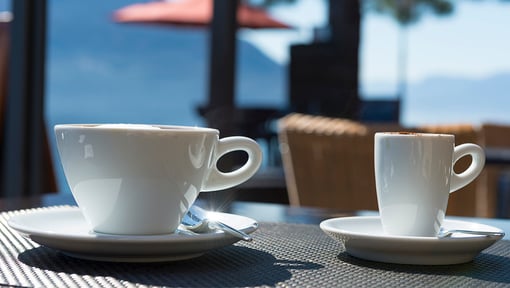 Two white coffee cups on saucers placed on a table outdoors