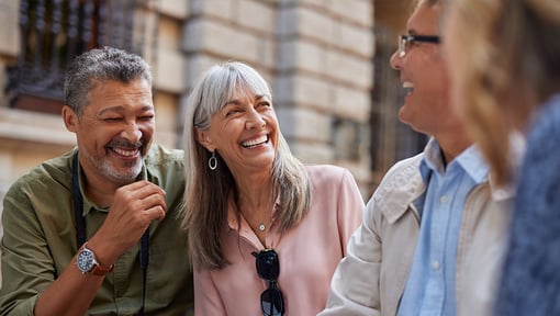 Two older adults laughing with some friends, they are in a good mood.