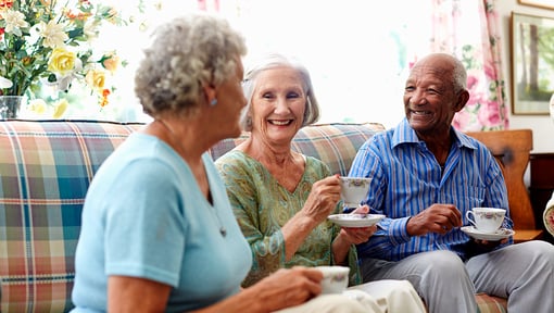 Three senior aged people enjoying some social connection and having tea on the couch.