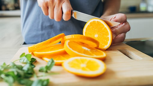 Someone cutting orange slices for a orange, avocado, spinach salad