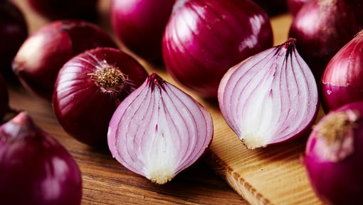 Antioxidant packed whole and halved red onion on a cutting board.