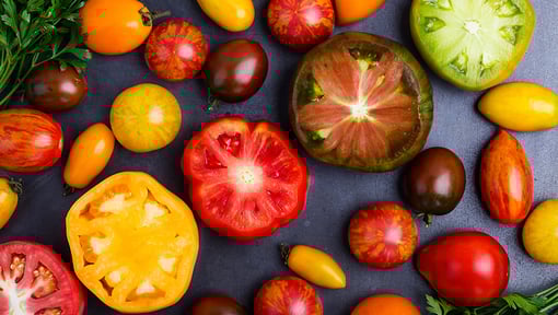 Different types of juicy nutritious tomatoes sliced and whole on a black table top. 
