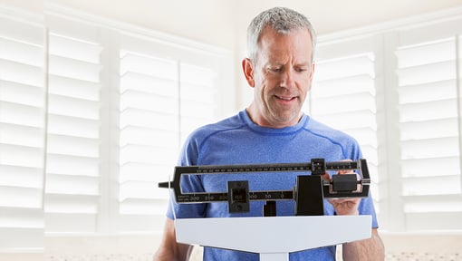 An adult standing on a bathroom scale in a bright room, checking their weight as part of a health or wellness routine.