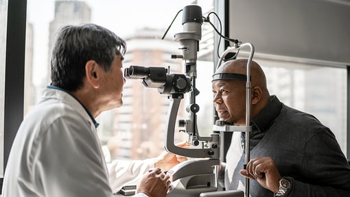 Eye care professional using a slit lamp microscope to examine a patient’s eyes in a clinical setting.