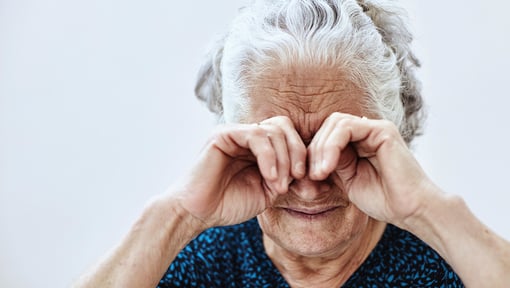 An older adult rubbing both eyes with hands, illustrating eye irritation or dry eye discomfort.