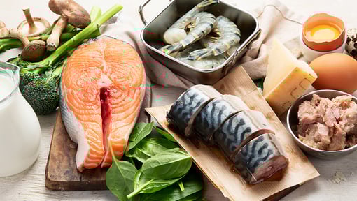 Assortment of foods that are dietary sources of vitamin D, including salmon, shrimp, eggs, milk, mushrooms, and leafy greens