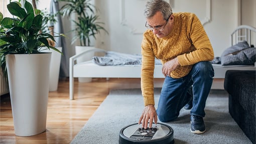 A older adult man turns on a robot vacuum cleaner