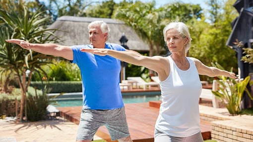 Two older adults practicing a somatic exercise outdoors, standing side by side with arms extended.