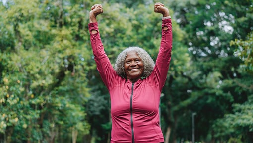 older adult woman lifting her arms in the air smiling at the camera. 