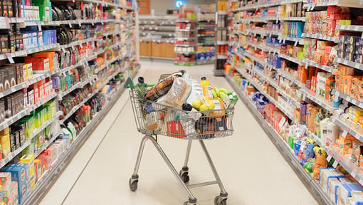 A full grocery cart in the middle of a grocery store isle. 