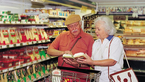 Two older adults in a grocery store reviewing the nutrition labels on the back of two food packages.