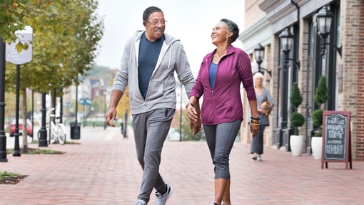 An older adult man and woman enjoying a outdoor walk on a sidewalk near local businesses. 