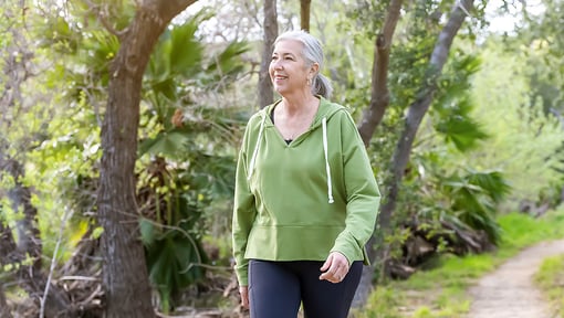 An older adult woman walking on a nature trail.