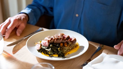 Plate of cooked meat served over greens and grains on a dining table-of-steak