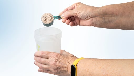 Hands holding a measuring scoop of powdered supplement above a plastic shaker cup