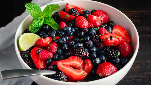 A berry mint fruit salad, that includes mint, strawberries, blackberries, raspberries, blueberries, and a slide of lime.