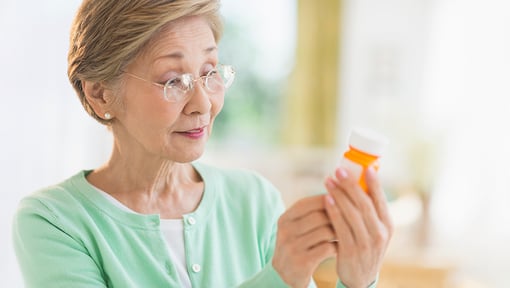 Older adult wearing glasses reviews a prescription medication bottle and label at home.