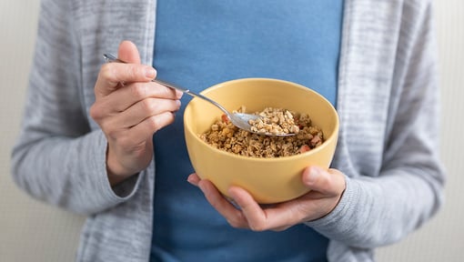 Person eating a bowl of fiber-rich cereal or granola, illustrating a healthy breakfast choice for digestive health.