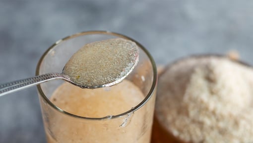 Fiber supplement on a spoon over a drinking glass filled with fiber and water