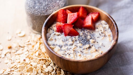 Bowl of oatmeal topped with sliced strawberries and chia seeds, surrounded by rolled oats and a jar of chia seeds.