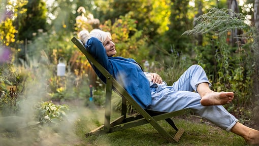 Older adult woman resting in a garden filled with plants and trees, highlighting the benefits of green spaces for stress reduction and brain health.