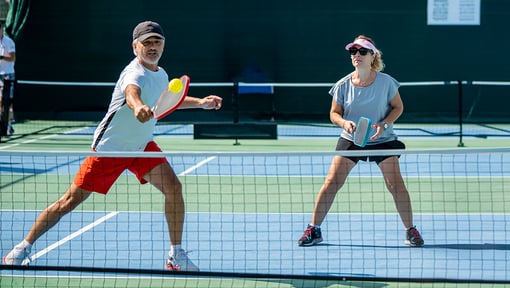 Two players positioned at the net during a doubles pickleball match on an outdoor court.