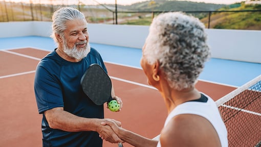 Two pickleball players shaking hands at the net after a game on an outdoor court.
