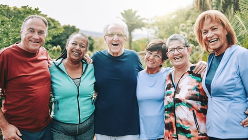 Group of older adults standing together outdoors with arms around one another.