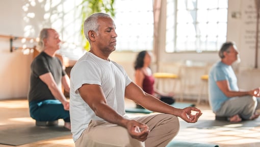 Adults practicing mindfulness meditation in a group wellness class at a fitness or community center.