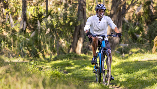 A man riding a bicycle along a trail through a wooded outdoor area.
