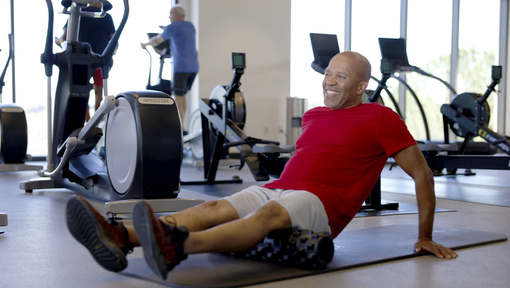 An older adult using a foam roller on a workout mat in a gym for recovery. 